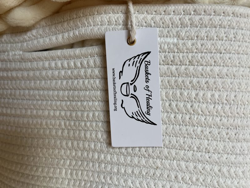 A Baskets of Healing tag with the winged-basket logo tied to a cream rope basket